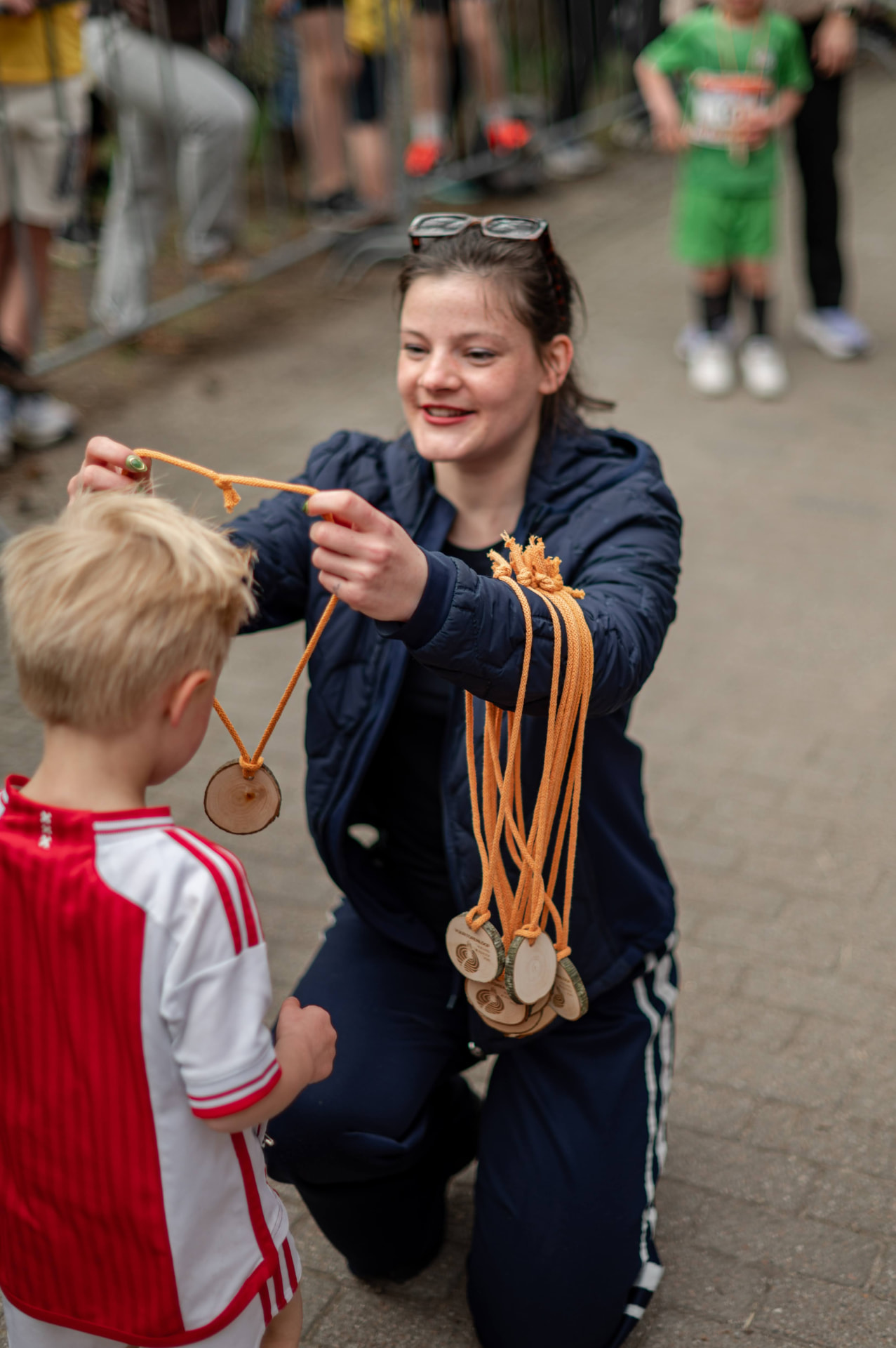 Vrijwilliger hangt een houten medaille om een jonge deelnemer